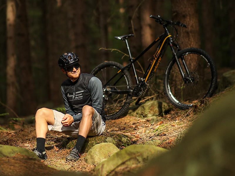Cycliste assis sur un rocher, à côté d'un vélo électrique de montagne 4EVER. 