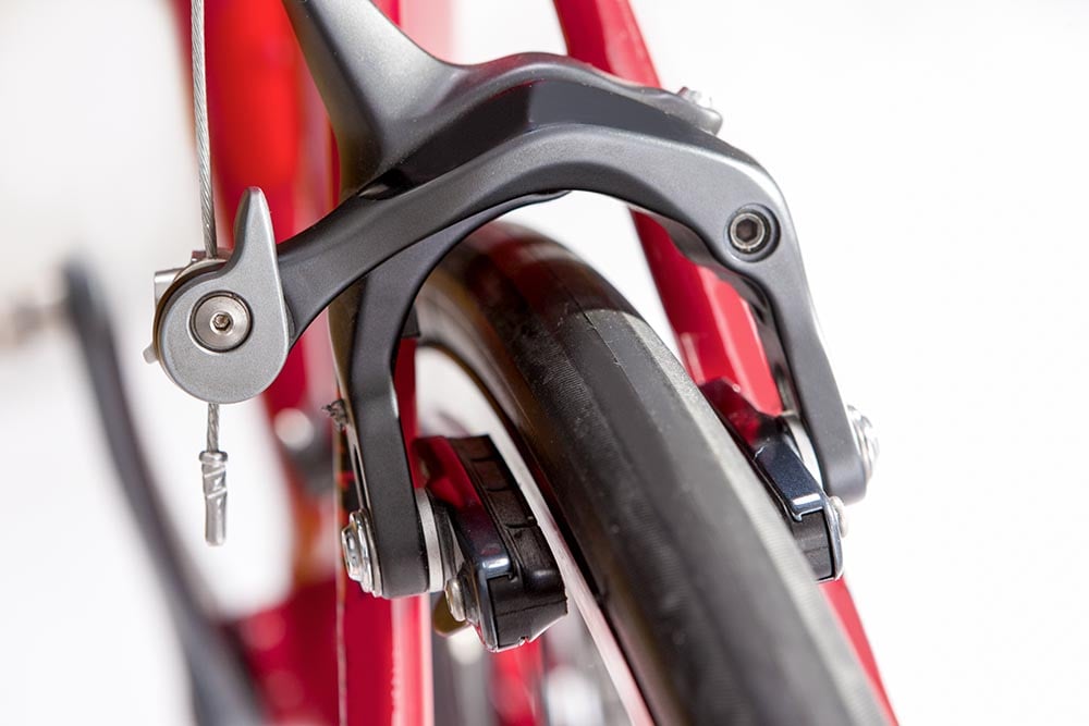 Detailný pohľad na čeľusťové brzdy priložené k ráfiku kolesa bicykla.